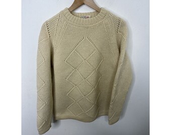 Peut inclure: Un pull en tricot crème avec un motif en losanges. Le pull a un col rond et des manches longues.