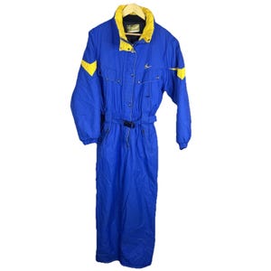 May include: A blue and yellow ski suit. The one-piece suit features a high collar, a belt at the waist, and yellow accents on the shoulders and sleeves. The suit is made of a water-resistant material, designed for cold weather activities.