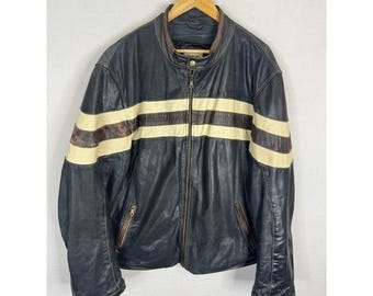 Peut inclure: Veste en cuir noir avec des rayures crème sur la poitrine et les bras. La veste a une fermeture éclair, deux poches latérales et un col marron. Elle est suspendue à un cintre en bois.