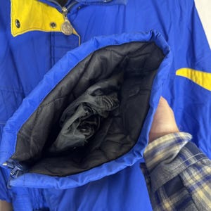 May include: A blue and yellow winter jacket with a black quilted lining. The jacket has a zip closure and a high collar. The sleeve is open, revealing the black lining and a drawstring cuff.