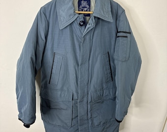 Peut inclure: Une veste matelassée bleu à manches longues avec une fermeture éclair noire et des bordures noires. La veste a deux grandes poches sur le devant et une petite poche sur la manche gauche. La veste porte une étiquette avec l'inscription "Scuba".