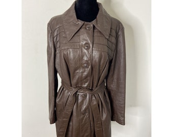 May include: A brown leather jacket with a belt and button closure. The jacket has a collar and long sleeves.