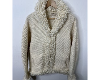 May include: A white knitted cardigan with a fluffy collar and button closure. The cardigan has two pockets and a "Mountain" label.