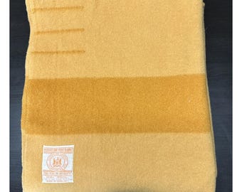 Peut inclure: Une couverture en laine jaune moutarde avec une large bande horizontale d'une teinte jaune plus foncée et trois courtes lignes horizontales près du bord supérieur. Une étiquette rectangulaire blanche est cousue dans le coin avec le texte Hudson's Bay Point Blanket.