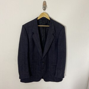 Op de afbeelding: Een zwart blazer met een subtiel gestreept patroon. De blazer heeft een enkele knoopsluiting en twee zakken.
