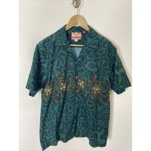 Könnte beinhalten: Ein grünes, kurzärmeliges Hemd mit Knöpfen und einem Blumenmuster. Das Hemd hat einen Kragen und eine Tasche auf der linken Seite. Das Etikett auf dem Hemd lautet "RJC".