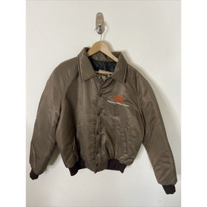 May include: A brown satin bomber jacket with a snap closure and a brown ribbed knit collar, cuffs, and waistband. The jacket has an embroidered logo that reads "Highland Valley Copper".