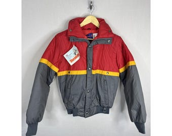 May include: A vintage red, gray, and yellow winter jacket with a high collar and snap closures. The jacket has a red upper section, gray lower section, and a yellow stripe. A tag that says "Stormking" is attached.