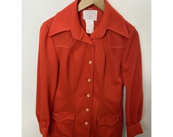 May include: A bright orange blazer with a pointed collar, long sleeves, and a button-up front. The blazer has two pockets on the front and a white label with the text "Jo-Linda" on the inside.