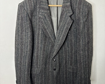 May include: A brown and gray herringbone patterned blazer with a single-breasted closure and three buttons. The blazer has a notched lapel and two flap pockets.