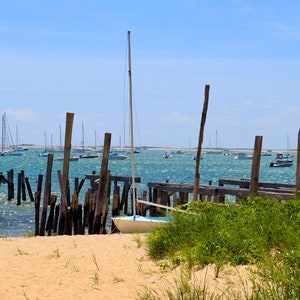 Puede incluir: Un velero blanco atracado en un muelle de madera en un día soleado. El muelle está parcialmente sumergido en el agua. Hay otros veleros en la distancia.