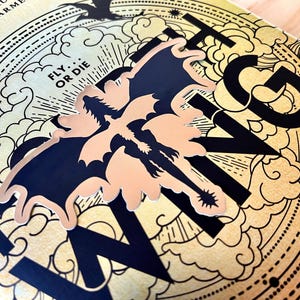 Puede incluir: Primer plano de una portada de libro con la palabra "WING" en letras negras grandes. Un gr&aacute;fico de drag&oacute;n en negro y melocot&oacute;n est&aacute; centrado en la portada. El fondo es dorado con un dise&ntilde;o de nubes y l&iacute;neas. El texto "FLY OR DIE" tambi&eacute;n es visible.