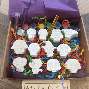 May include: A craft kit containing white ceramic figurines of Harry Potter characters, paint, brushes, and colourful tissue paper in a box. The box has a label that says "Arty Kids Creations - Play - Paint - Create".