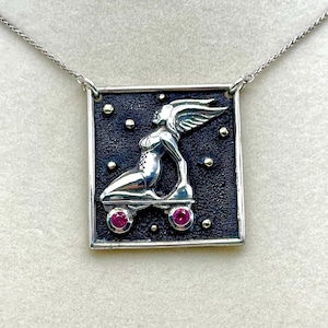 May include: A silver pendant necklace with a square-shaped charm featuring a winged figure on roller skates. The charm has a black background with gold accents and two pink gemstones.