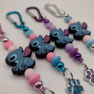May include: Several keychains featuring a blue cartoon character with large ears and a paw print charm. The keychains have a variety of colorful beads in pink, blue, and purple. Each keychain has a silver clasp.