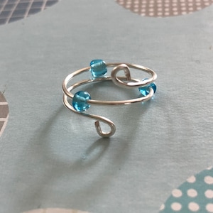 May include: A silver ring with a twisted design and blue glass beads.