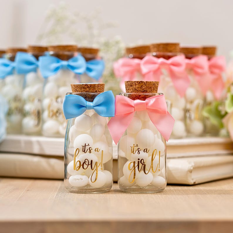 K&ouml;nnte beinhalten: Gl&auml;ser gef&uuml;llt mit wei&szlig;en Bonbons, mit Korken und Schleifen versehen. Ein Glas hat eine blaue Schleife und sagt "it's a boy!" in goldener Schrift. Ein anderes hat eine rosa Schleife und sagt "it's a girl!"