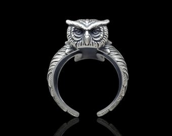 May include: A silver-toned metal ring featuring a detailed owl head design at the top. The band of the ring is shaped like stylized owl wings that wrap around, with an open back design. The metal has a polished finish with dark recessed areas.