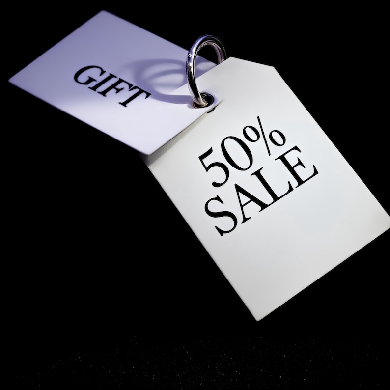May include: Two white gift tags with a silver ring. One tag reads "GIFT" in black, the other reads "50% SALE" in black. The background is black.