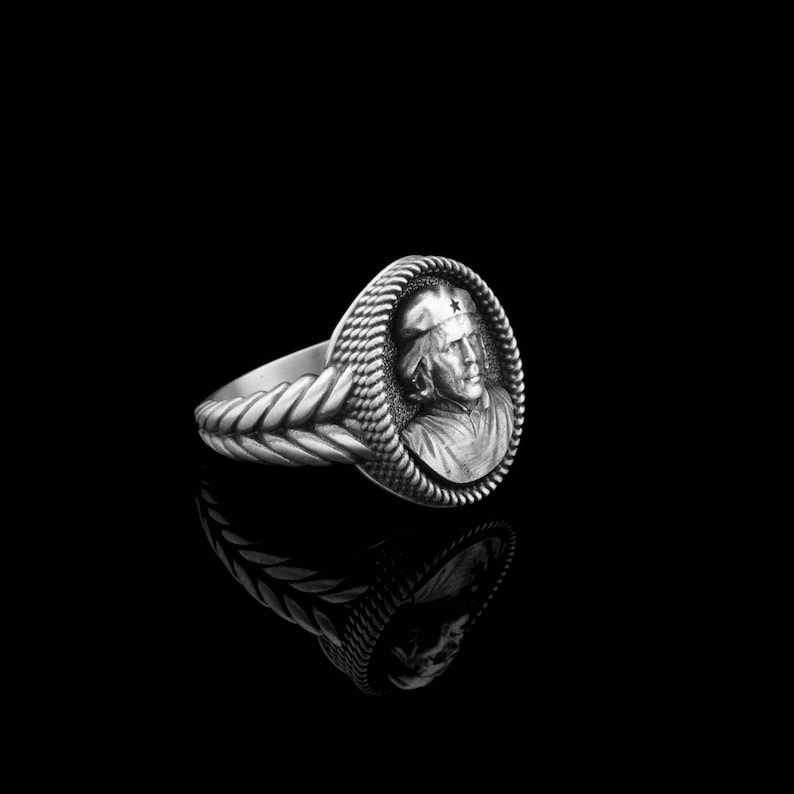 May include: A silver ring with a braided band and a round, raised cameo featuring a person wearing a cap with a star.