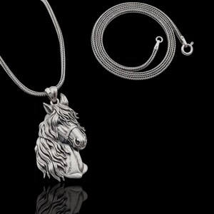 Puede incluir: Un collar con colgante plateado que presenta un dise&ntilde;o detallado de cabeza de caballo. La melena y los rasgos faciales del caballo est&aacute;n intrincadamente esculpidos. La cadena del collar es plateada y el fondo es negro.