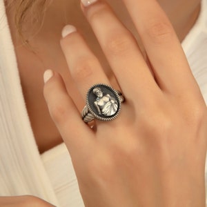 Puede incluir: Un anillo de plata con un camafeo ovalado detallado que presenta una figura esculpida de un hombre. El anillo tiene un dise&ntilde;o de cuerda alrededor del borde del camafeo.
