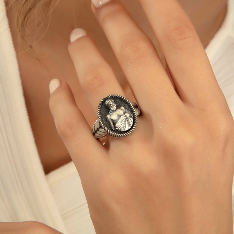 Puede incluir: Un anillo de plata con un camafeo ovalado detallado que presenta una figura esculpida de un hombre. El anillo tiene un dise&ntilde;o de cuerda alrededor del borde del camafeo.
