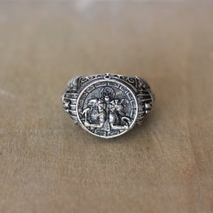 Op de afbeelding: Een zilveren ring met een ingewikkeld ontwerp met een mythisch wezen. De ring heeft een ronde band met een reli&euml;f van een wezen met vleugels en een kroon.