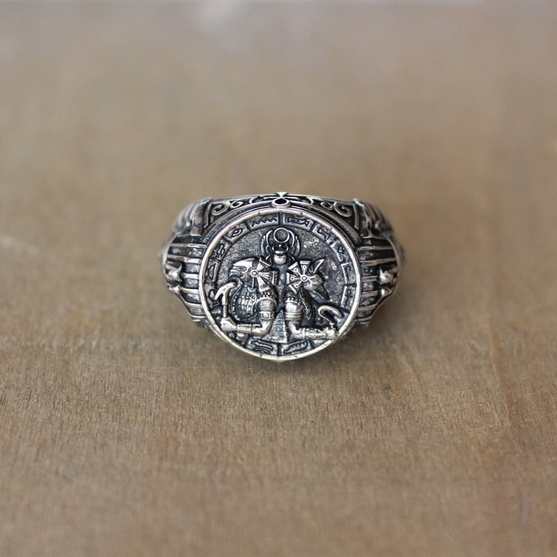 Op de afbeelding: Een zilveren ring met een ingewikkeld ontwerp met een mythisch wezen. De ring heeft een ronde band met een reli&euml;f van een wezen met vleugels en een kroon.
