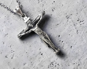 Peut inclure: Pendentif crucifix argenté avec une représentation détaillée de Jésus-Christ sur la croix. Le pendentif est suspendu à une chaîne délicate. Le fond est une surface grise texturée.