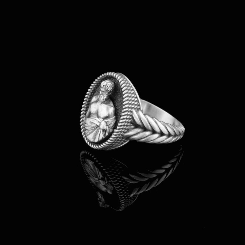 Puede incluir: Un anillo de plata con un dise&ntilde;o detallado. El anillo presenta un &oacute;valo elevado con una figura esculpida de un hombre que lleva una corona. La banda del anillo est&aacute; trenzada.