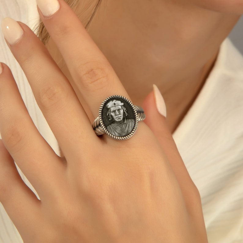 May include: A silver ring with a black and white portrait of a person wearing a hat. The ring has a rope-like design around the edge.