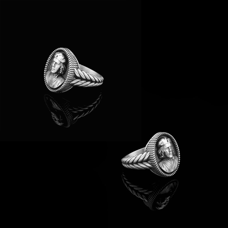 May include: Two silver rings with a detailed design of a person's face on the front. The rings are on a black background.
