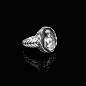 Puede incluir: Un anillo de plata con un dise&ntilde;o detallado que presenta un busto de hombre en el centro. El anillo tiene una banda trenzada.