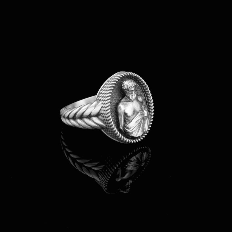 Puede incluir: Un anillo de plata con un dise&ntilde;o detallado que presenta un busto de hombre en el centro. El anillo tiene una banda trenzada.