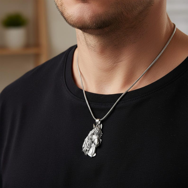 Puede incluir: Collar con colgante de caballo plateado. El colgante presenta una cabeza de caballo detallada con una melena fluida. El collar se lleva en una cadena plateada sobre una camiseta negra. Una joya &uacute;nica.
