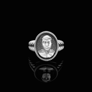 May include: A silver ring with a rope-like band and an oval cameo featuring a man's face.