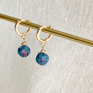 Può includere: Un paio di orecchini a cerchio dorati con una pietra preziosa blu e rosa che pendono da ogni cerchio.