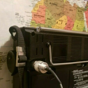 May include: A black portable radio with a silver metal handle and a black strap. The radio has a black and silver antenna and a black speaker grille. The radio is sitting on a map.