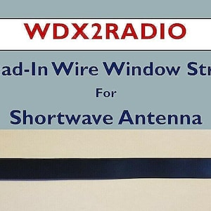 Puede incluir: Una correa de ventana Lead-In Wire negra para antena de onda corta. La correa tiene una base de cobre con una correa negra y está asegurada con tornillos plateados y extremos de plástico azul. El texto "WDX2RADIO" está en la parte superior.
