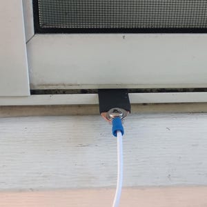 May include: A white window with a black screen and a white cable with a blue connector. The cable is connected to a metal piece secured with a screw and covered with black tape.