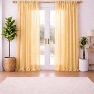 May include: A bright, airy interior scene featuring sheer yellow curtains framing a white double door. The curtains hang from a gold rod. A large beige rug sits on the wooden floor. Potted plants flank the door, adding a touch of greenery.