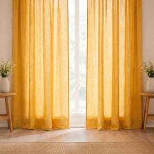 May include: Two golden yellow linen curtains frame a window, with a natural woven rug on the floor. The long, flowing curtains create a warm atmosphere. Small wooden side tables with white vases and flowers are on either side of the window, adding a touch of elegance.