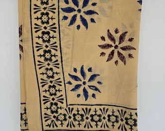 May include: A tan fabric scarf with a floral pattern in navy blue and maroon. The scarf is hanging on a wooden hanger. The border features a repeating black floral design.