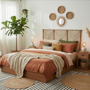 Puede incluir: Dormitorio con estructura de cama de madera, edredón color terracota y manta de punto crema. La cama está adornada con varias almohadas decorativas. Una cabecera de macramé y decoraciones de pared completan el estilo bohemio.