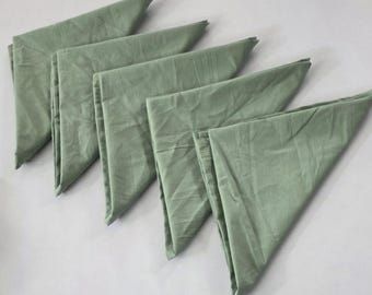 May include: Six sage green cloth napkins, arranged in a fan shape. The napkins are folded into triangles, with visible creases and a slightly textured appearance. The fabric has a soft, matte finish.