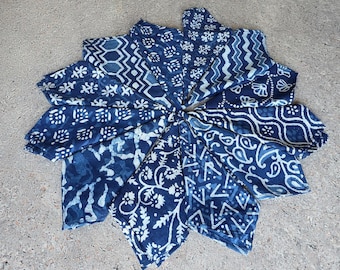 Puede incluir: Un conjunto de servilletas de tela azul índigo y blanca estampadas, dispuestas en forma circular. Cada servilleta presenta un diseño único, incluyendo motivos florales, geométricos y de cachemira. Las servilletas están hechas de un material suave, probablemente natural.