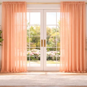 Puede incluir: Una habitación luminosa y espaciosa con cortinas transparentes de color melocotón que enmarcan una puerta francesa. Las cortinas cuelgan de una barra dorada. Una alfombra grande y plantas en macetas, incluyendo una higuera de hoja de violín, completan la decoración.