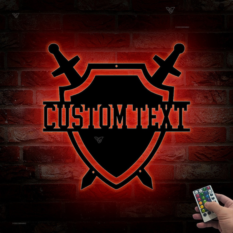 May include: A black metal shield with two swords crossed behind it. The shield has the text "CUSTOMTEXT" written across the center. The shield is illuminated with red light. A remote control is visible in the bottom right corner.
