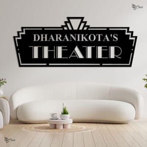May include: Black metal wall art sign that reads "DHARANIKOTA'S THEATER" in a stylized font. The sign has an art deco design and is mounted on a white wall above a white sofa. The sign is a decorative piece.